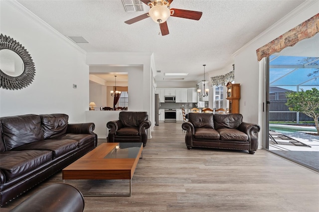 living area with crown molding, visible vents, light wood-style flooring, and ceiling fan with notable chandelier