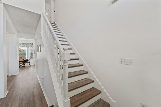 stairs with wood finished floors, an inviting chandelier, and baseboards
