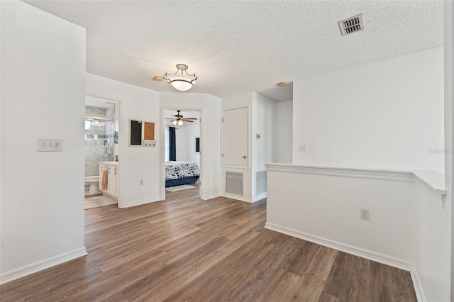 interior space featuring a textured ceiling, wood finished floors, baseboards, and visible vents