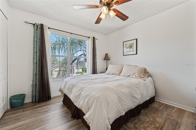 bedroom with a textured ceiling, baseboards, a ceiling fan, and wood finished floors
