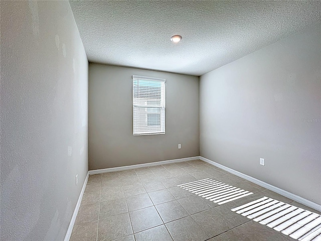 spare room with light tile patterned floors, baseboards, and a textured ceiling