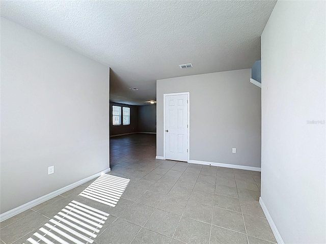 unfurnished room featuring tile patterned flooring, visible vents, a textured ceiling, and baseboards