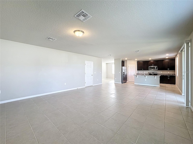 unfurnished living room with light tile patterned floors, visible vents, a textured ceiling, and baseboards
