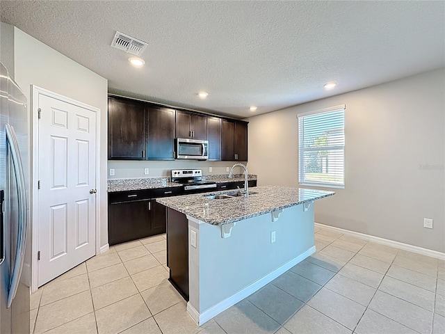kitchen with a breakfast bar area, light stone counters, visible vents, a sink, and stainless steel appliances
