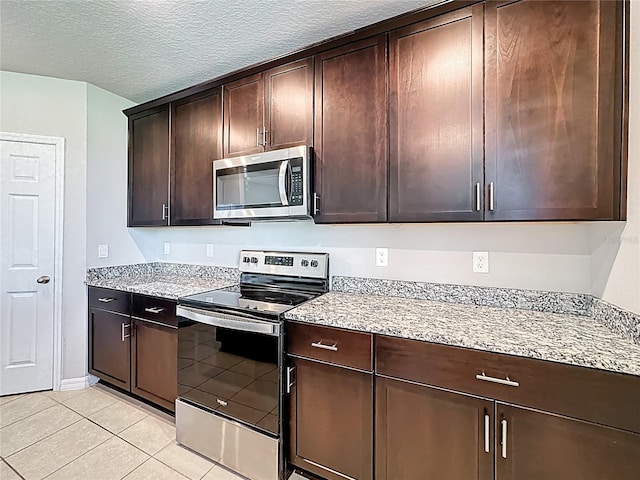 kitchen with light tile patterned floors, light stone countertops, stainless steel appliances, dark brown cabinets, and a textured ceiling