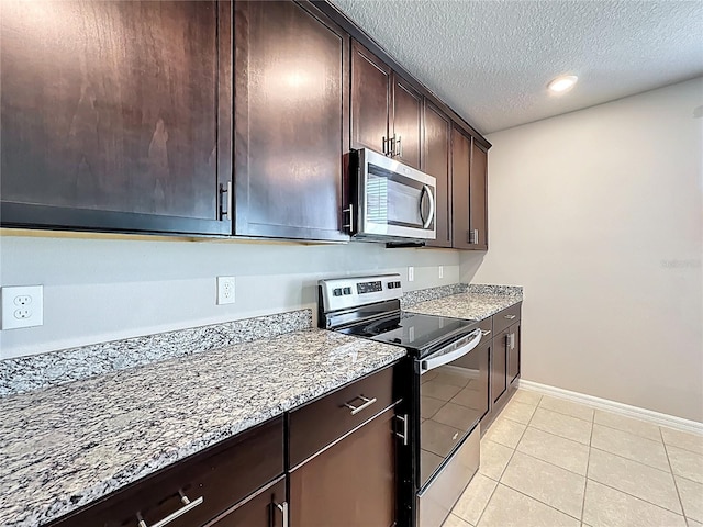 kitchen with light stone counters, light tile patterned floors, dark brown cabinets, appliances with stainless steel finishes, and a textured ceiling