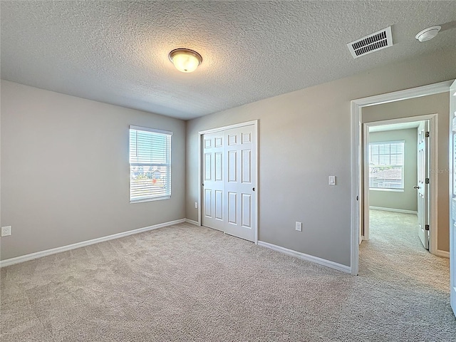 unfurnished bedroom featuring a closet, visible vents, multiple windows, and carpet