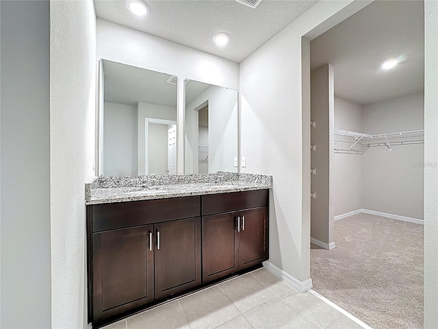 full bath featuring a walk in closet, double vanity, baseboards, and a sink