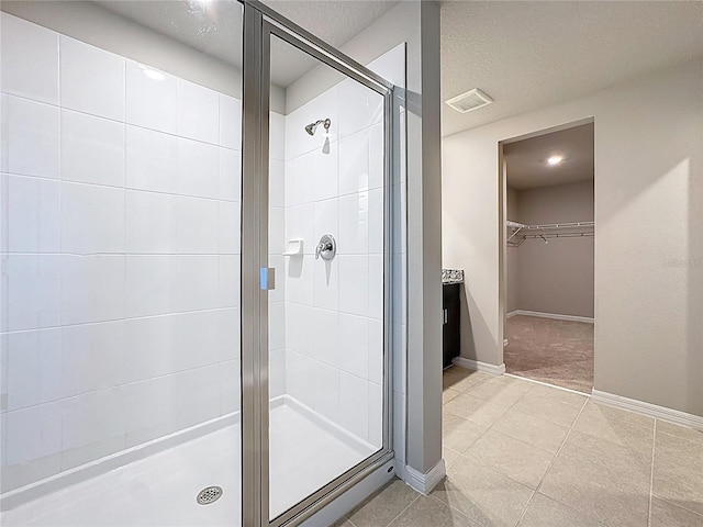 bathroom with visible vents, a textured ceiling, a shower stall, baseboards, and a spacious closet