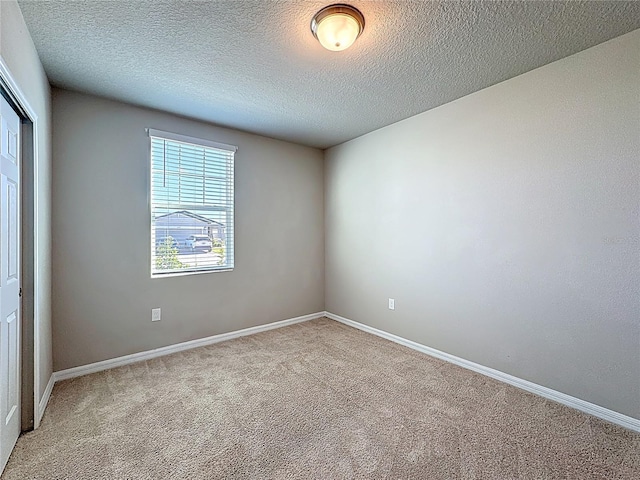 empty room featuring baseboards, light carpet, and a textured ceiling