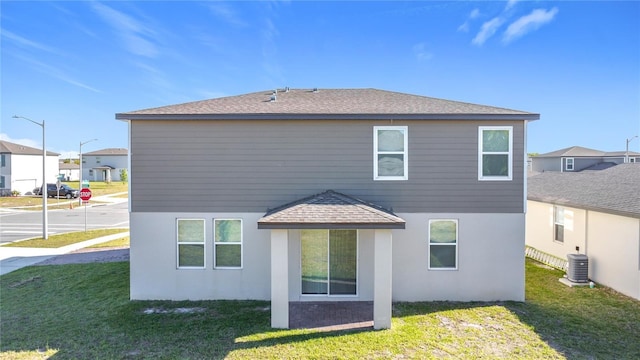 back of property with a yard, central air condition unit, stucco siding, and a shingled roof