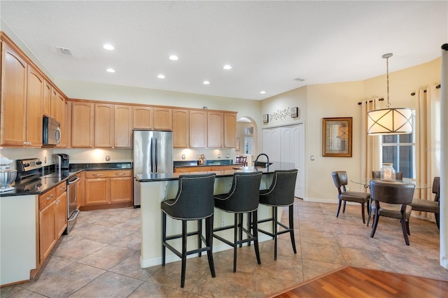 kitchen featuring a breakfast bar area, a center island with sink, visible vents, arched walkways, and appliances with stainless steel finishes