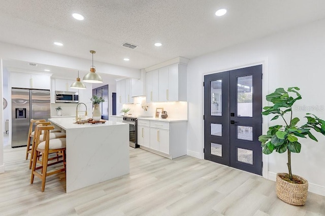 4907 21st Ave W, Bradenton, FL 34209 - kitchen featuring a kitchen island with sink, light wood-style flooring, stainless steel appliances, light countertops, and hanging light fixtures