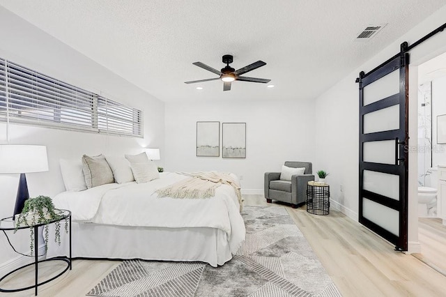 4907 21st Ave W, Bradenton, FL 34209 - bedroom with light wood-type flooring, visible vents, a textured ceiling, a barn door, and baseboards