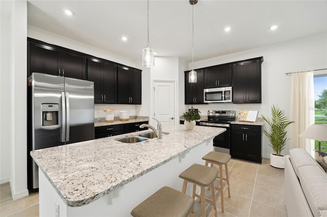 kitchen featuring appliances with stainless steel finishes, dark cabinetry, a kitchen breakfast bar, and a sink