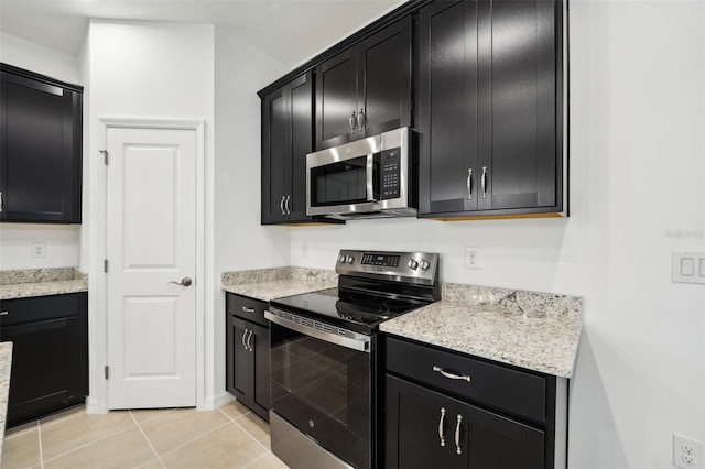 kitchen with light tile patterned floors, light stone counters, appliances with stainless steel finishes, and dark cabinets