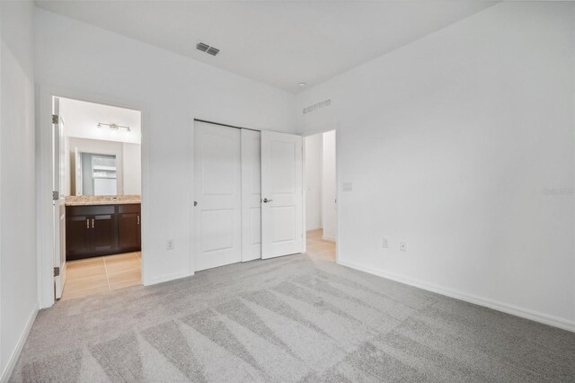 unfurnished bedroom with visible vents, baseboards, a closet, ensuite bathroom, and light colored carpet