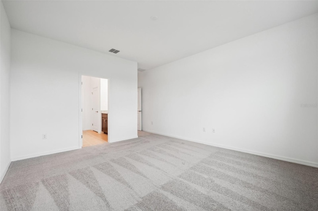 unfurnished bedroom with ensuite bath, light colored carpet, visible vents, and baseboards