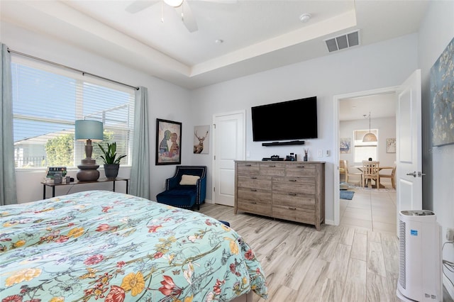 bedroom with light wood-type flooring, a tray ceiling, multiple windows, and visible vents