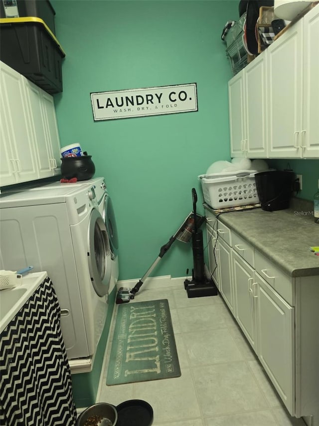 clothes washing area with washer and dryer, light tile patterned flooring, and cabinet space