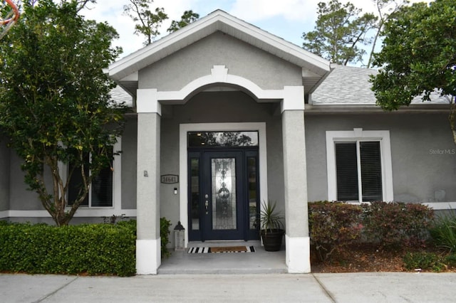 doorway to property with a shingled roof and stucco siding