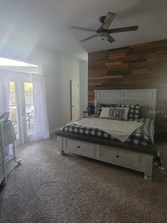 carpeted bedroom with wood walls, access to exterior, and a ceiling fan