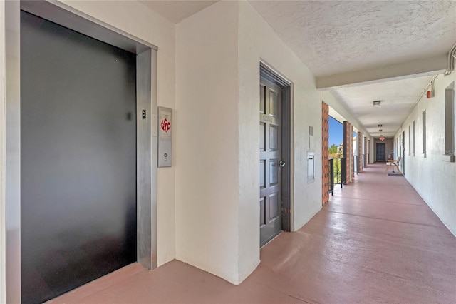 corridor featuring elevator, concrete flooring, and a textured ceiling