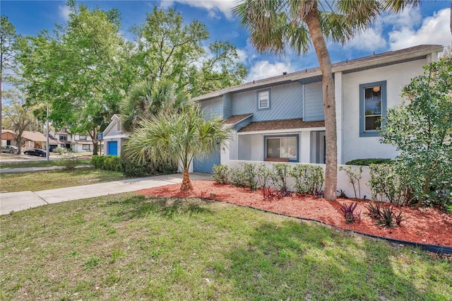 view of front of house with a front lawn, an attached garage, driveway, and stucco siding