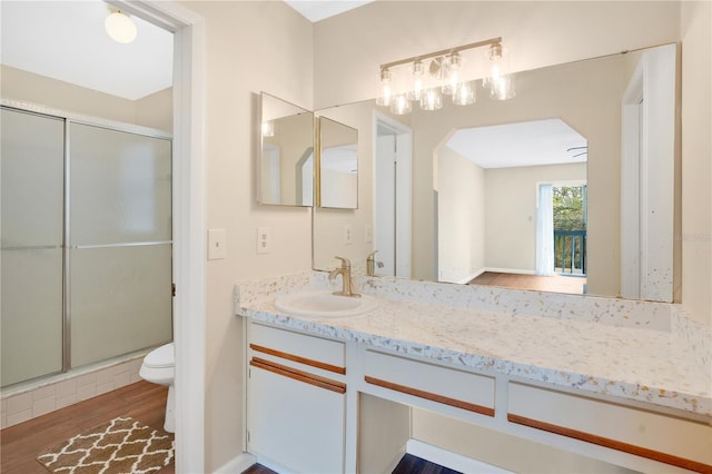 bathroom featuring vanity, toilet, wood finished floors, and a stall shower