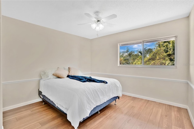 bedroom with ceiling fan, baseboards, a textured ceiling, and wood finished floors