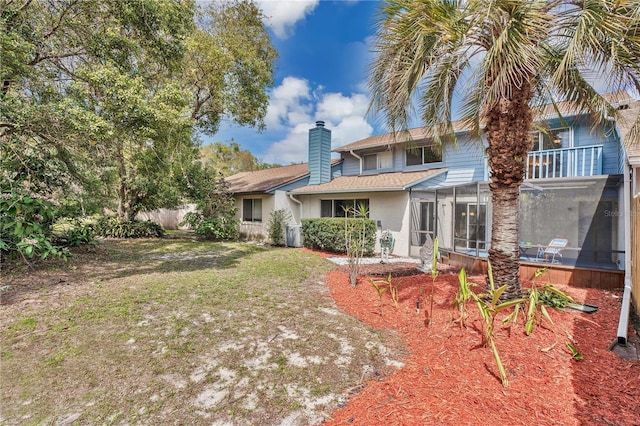 back of property featuring a balcony, roof with shingles, a yard, a sunroom, and a chimney