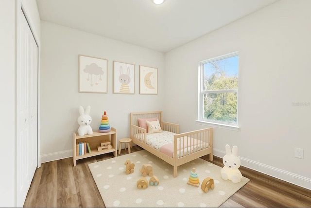 bedroom featuring wood finished floors, baseboards, and a crib