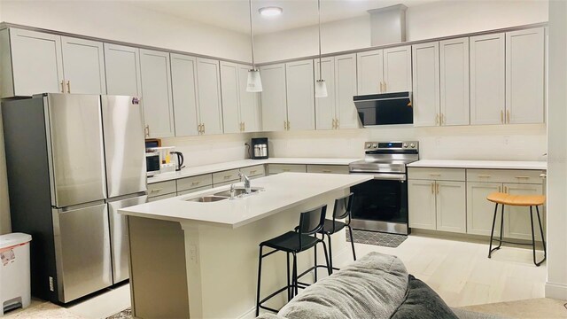 kitchen with pendant lighting, a kitchen bar, light countertops, stainless steel appliances, and a sink