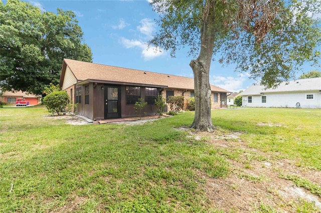 1148 Monroe Ave, Saint Cloud, FL 34769 - rear view of house with a sunroom, a yard, roof with shingles, and brick siding