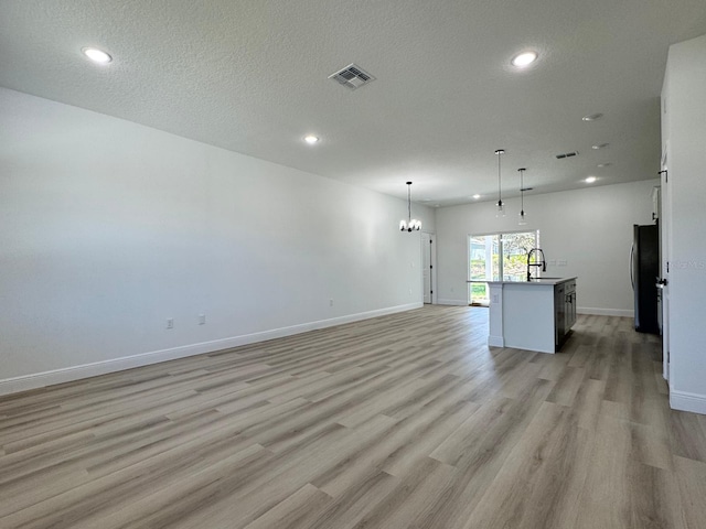 unfurnished living room with visible vents, baseboards, an inviting chandelier, and light wood finished floors