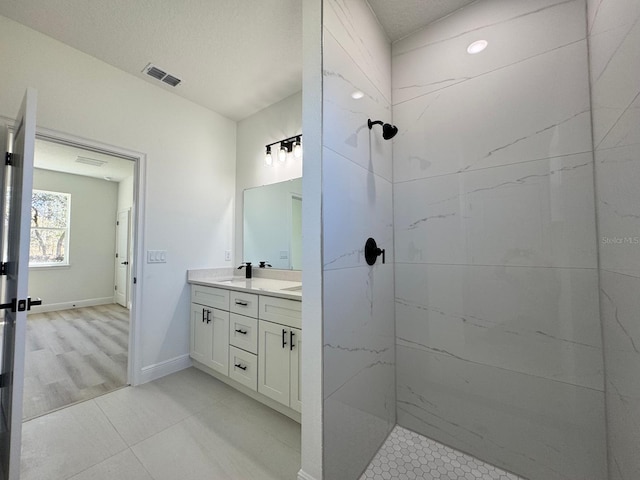 full bath with baseboards, visible vents, double vanity, a tile shower, and a sink