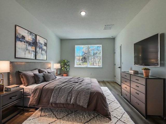 bedroom with visible vents, baseboards, a textured ceiling, and wood finished floors