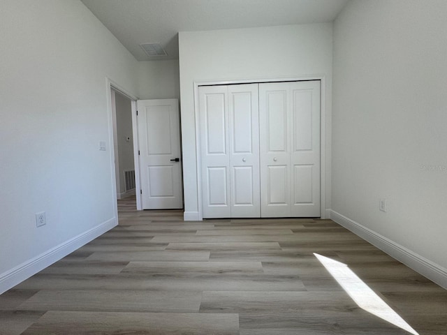 unfurnished bedroom with a closet, visible vents, baseboards, and wood finished floors