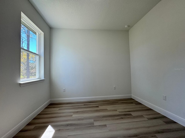 empty room with baseboards, a textured ceiling, and wood finished floors