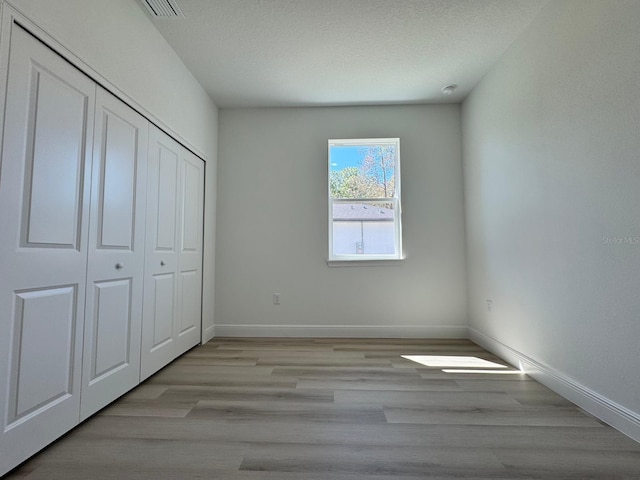 unfurnished bedroom featuring visible vents, baseboards, light wood finished floors, a closet, and a textured ceiling