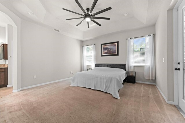 bedroom with a raised ceiling, light carpet, baseboards, visible vents, and arched walkways