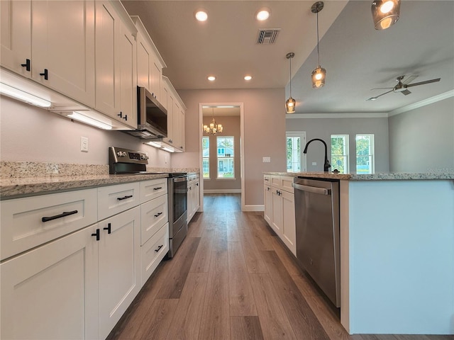 311 W Delaware Ave, Lake Helen, FL 32744 - kitchen with stainless steel appliances, wood finished floors, white cabinets, ornamental molding, and a chandelier