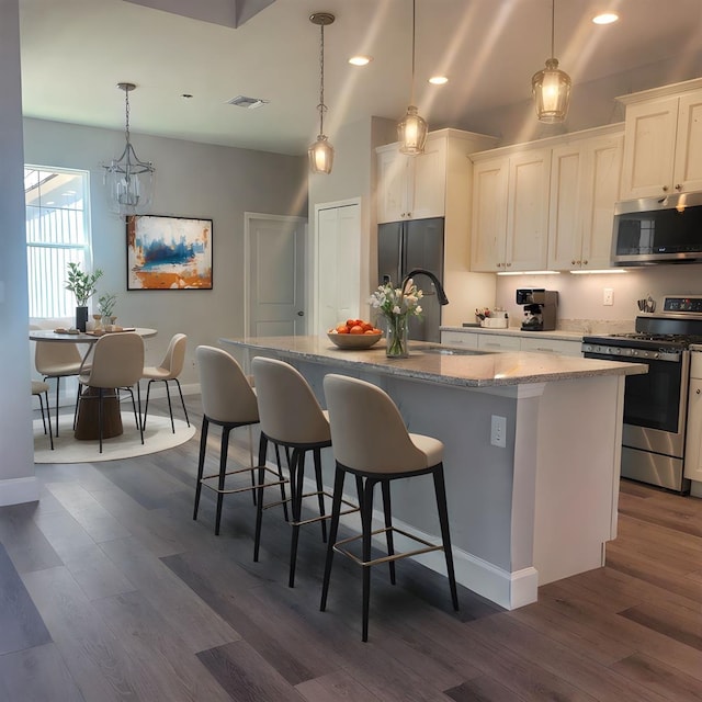 311 W Delaware Ave, Lake Helen, FL 32744 - kitchen featuring appliances with stainless steel finishes, a kitchen island with sink, dark wood-type flooring, light stone counters, and a chandelier