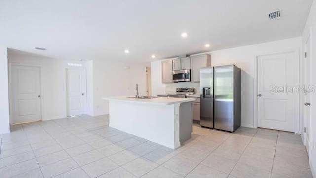 kitchen featuring gray cabinetry, a kitchen island with sink, a sink, stainless steel appliances, and light countertops