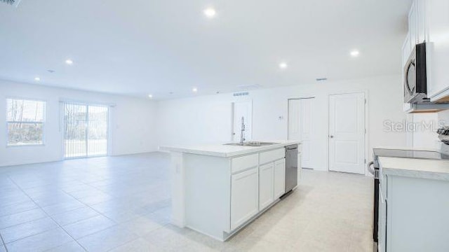 kitchen with an island with sink, a sink, open floor plan, stainless steel appliances, and light countertops