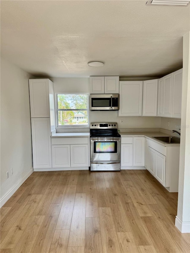 701 N 4th St, Haines City, FL 33844 - kitchen featuring light wood finished floors, a sink, white cabinets, and appliances with stainless steel finishes