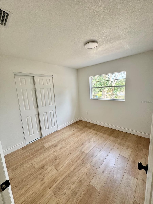 701 N 4th St, Haines City, FL 33844 - unfurnished bedroom featuring light wood-type flooring, baseboards, a textured ceiling, visible vents, and a closet
