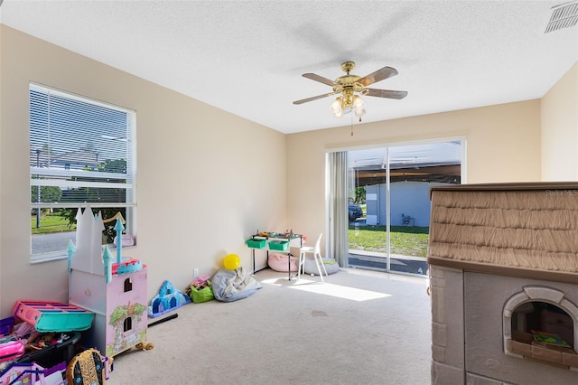 recreation room featuring visible vents, a textured ceiling, ceiling fan, and carpet floors