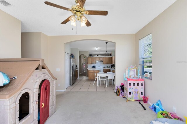 interior space featuring baseboards, visible vents, arched walkways, ceiling fan, and light colored carpet