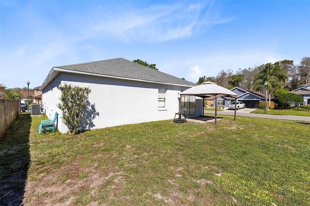 view of side of home with central air condition unit, a yard, fence, and stucco siding